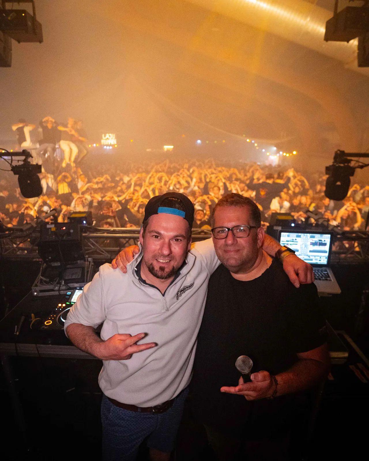 Soeren Hartmann und Basti van den Sroeden Seite an Seite auf der Bühne mit Crowd im Hintergrund, die Hände hochreißt.